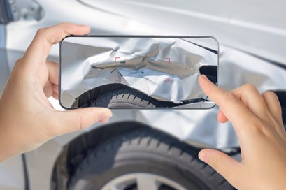 A person takes a photo of their dented car