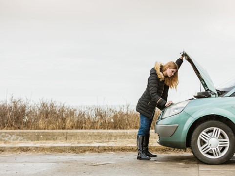 A woman looks under the bonnet of her non-running car following a breakdown.