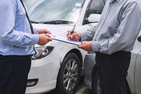 Two men signing a clipboard for selling a broken car for cash.