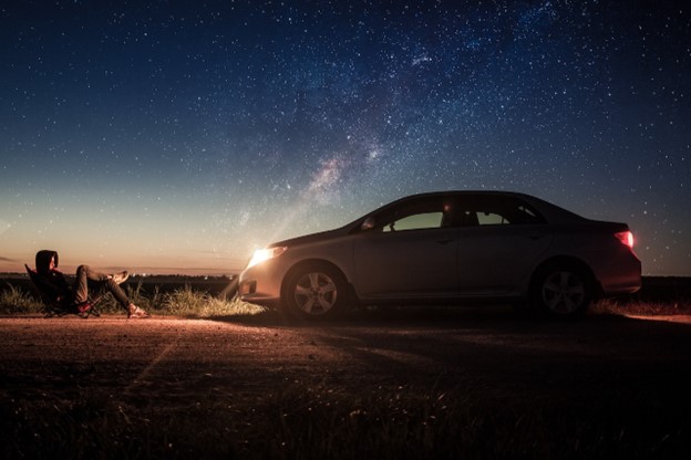 Person sitting in front of silver sedan at night